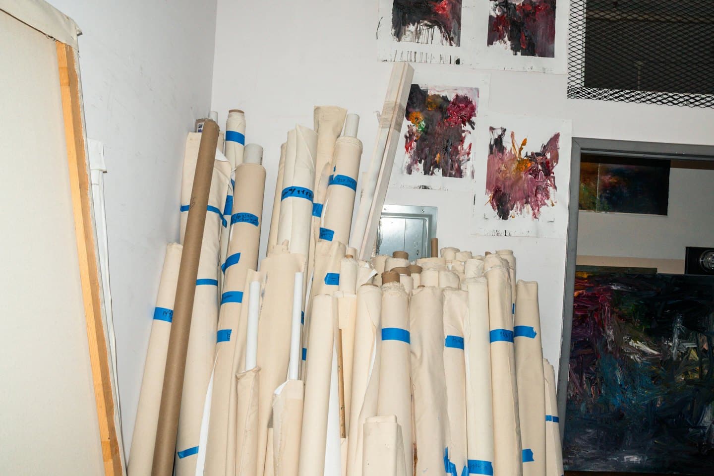Angolo di uno studio d'artista con rotoli di tela impilati e dipinti astratti.