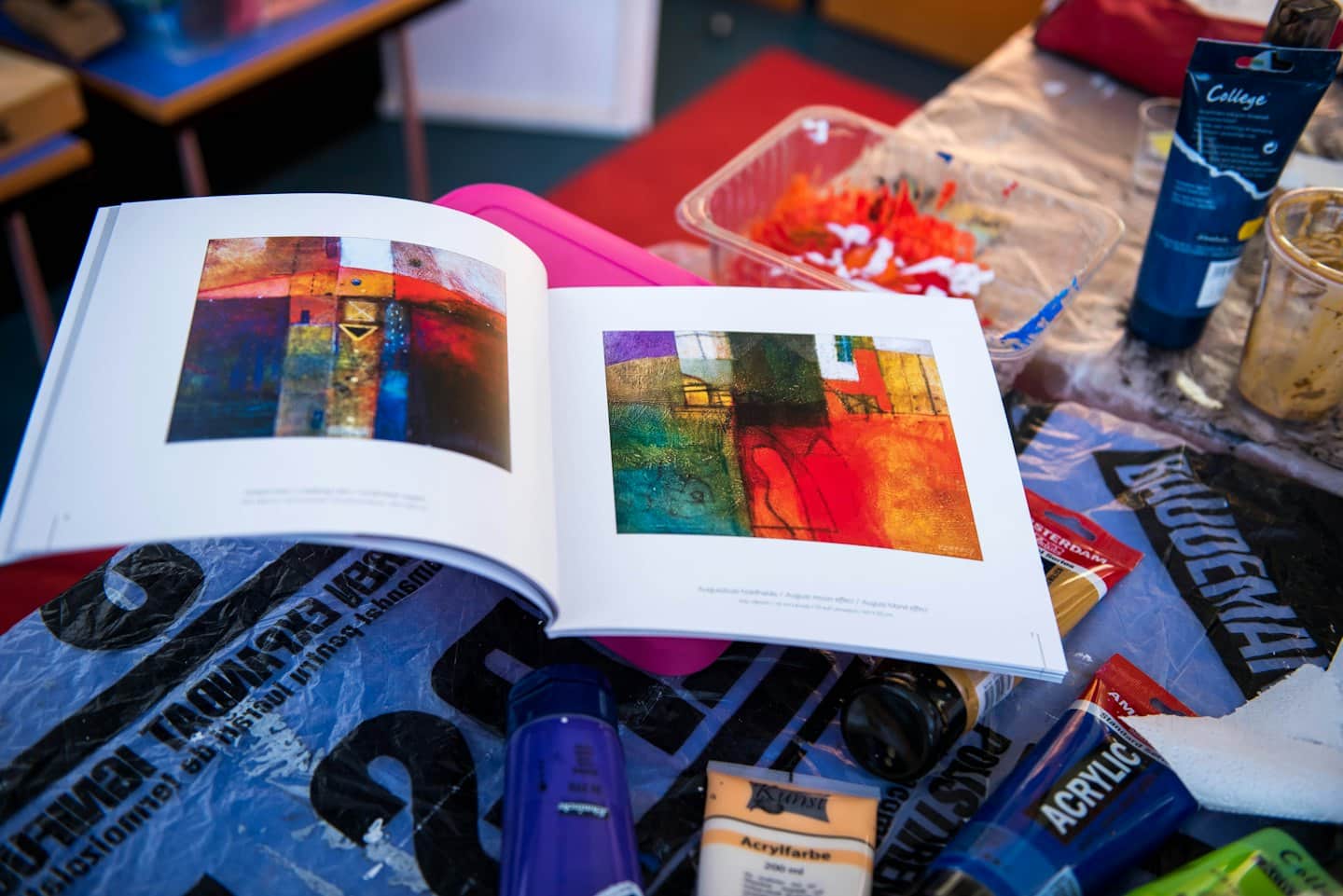 Un libro d'arte aperto appoggiato tra tubetti di colore acrilico.