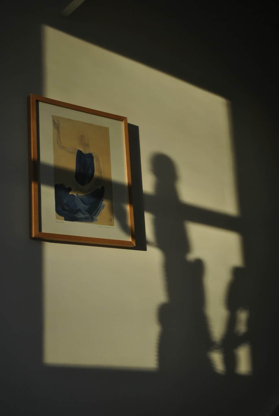 Quadro astratto con forme blu appeso a una parete illuminata dal sole.