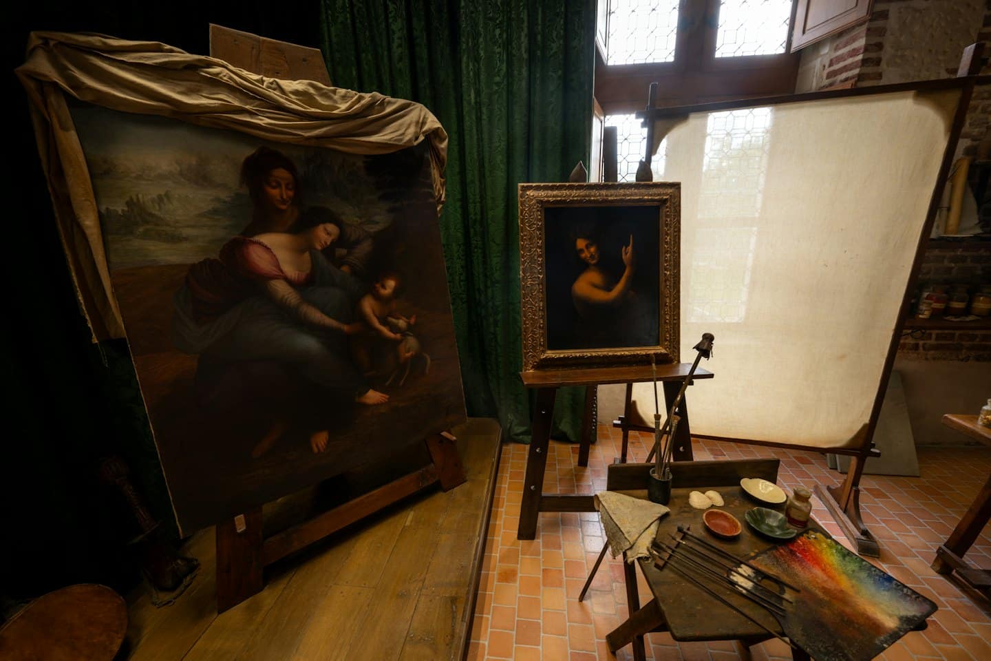 Studio d'artista con due dipinti a olio su cavalletti e materiale artistico su un tavolo.